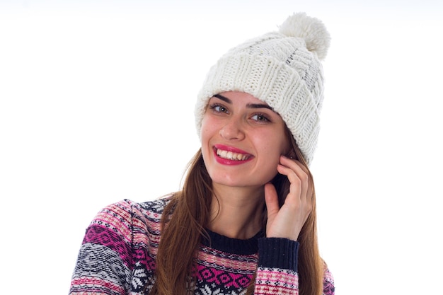 Giovane donna felice con i capelli lunghi in cappello bianco e maglione viola su sfondo bianco in studio