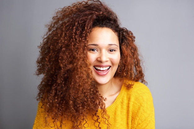 Giovane donna felice con i capelli ricci che ride sullo sfondo grigio