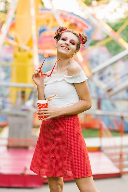 giovane donna felice con il trucco luminoso è in possesso di occhiali cerchiati rossi e divertirsi in un parco di divertimenti in estate
