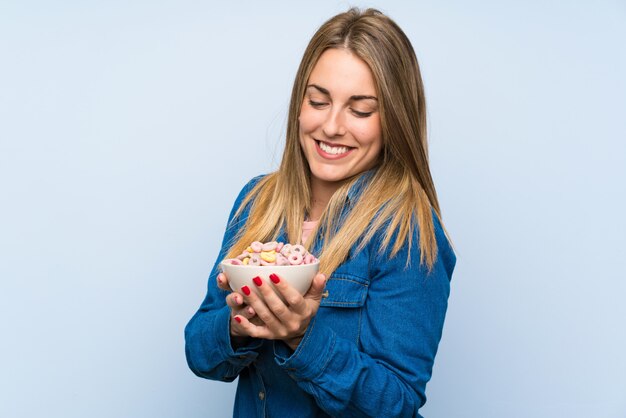 Giovane donna felice con la ciotola di cereali sopra la parete blu isolata