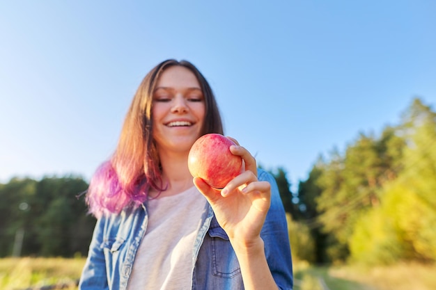 Giovane donna felice con la mela rossa, ragazza che morde una mela, sfondo del paesaggio naturale del tramonto, cibo naturale sano