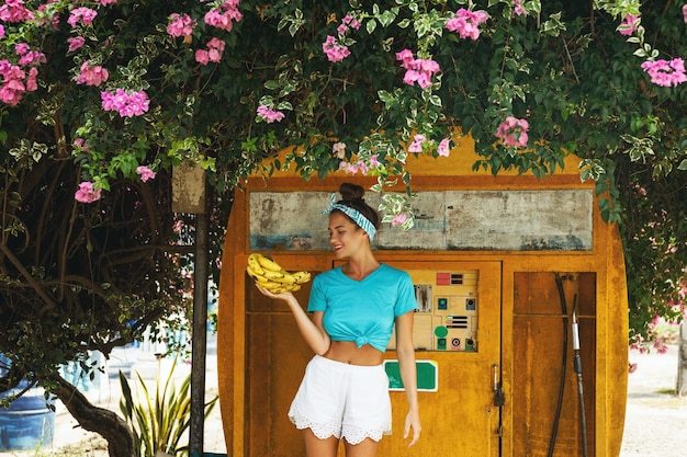 Giovane donna felice con un casco di banane in posa accanto alla vecchia stazione di servizio