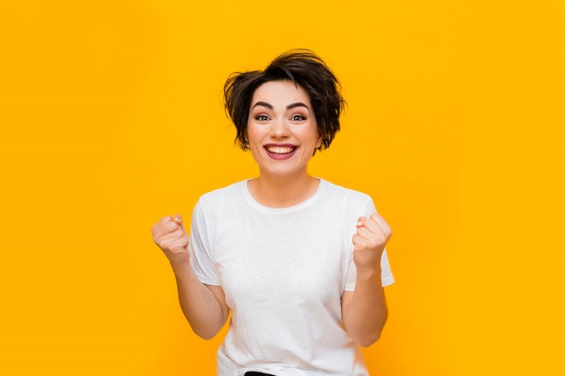 Giovane donna felice del brunette con un taglio di capelli corto in una maglietta bianca su una priorità bassa gialla. Ritratto di una giovane donna con varie emozioni su uno sfondo giallo. spazio per il testo