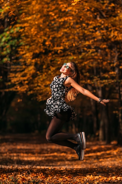 Giovane donna felice e allegra con un fantastico vestito che salta nella sosta di autunno