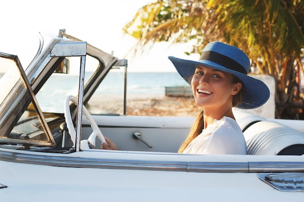 Giovane donna felice e retro automobile convertibile accanto alla spiaggia alla città di Varadero