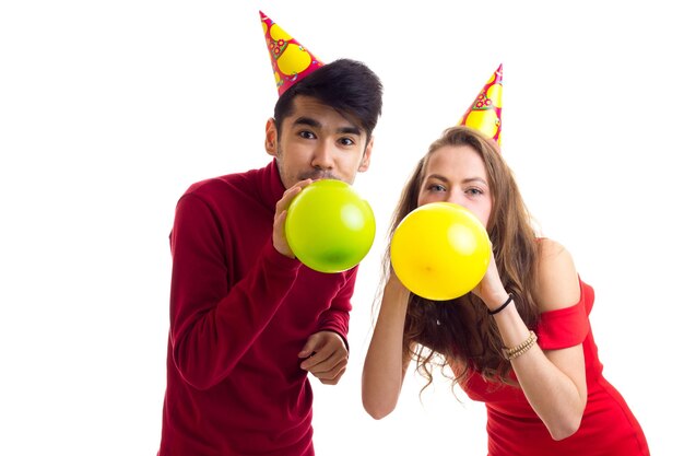 Giovane donna felice in abito rosso con cappello colorato e bell'uomo in camicia rossa che soffia palloncini