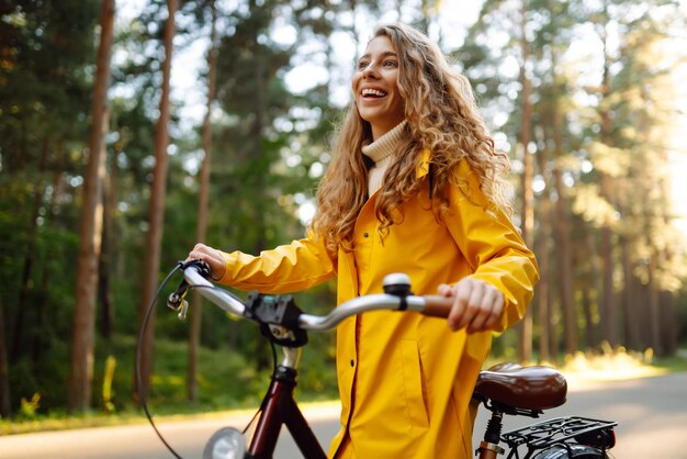 Giovane donna felice in cappotto giallo va in bicicletta nel parco soleggiato Rilassati il concetto di natura Stile di vita