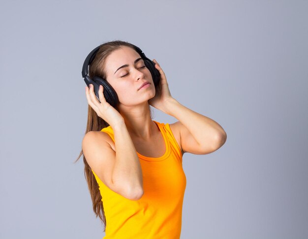 Giovane donna felice in maglietta gialla che ascolta la musica in cuffie nere in studio