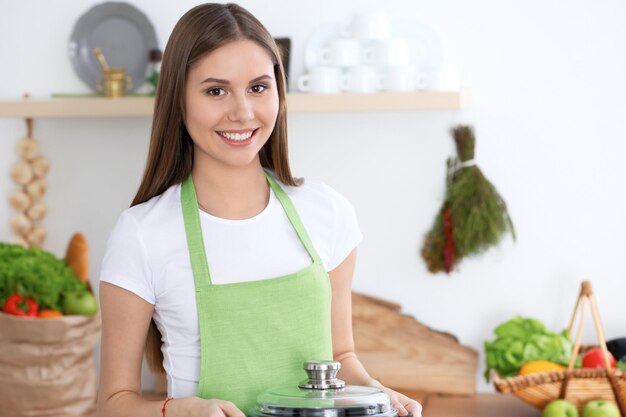 Giovane donna felice in un grembiule verde che cucina in cucina La casalinga ha trovato una nuova ricetta per la sua zuppa Cibo sano e concetto vegetariano