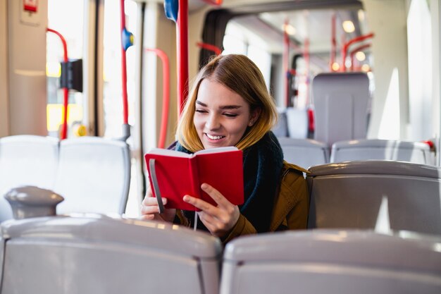 Giovane donna felice seduta in autobus urbano e leggendo un libro