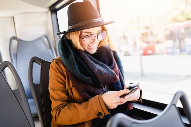 Giovane donna felice seduta in autobus urbano e utilizzando smart phone