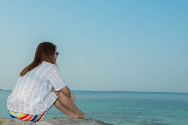 Giovane donna felice seduta sulla roccia in spiaggia