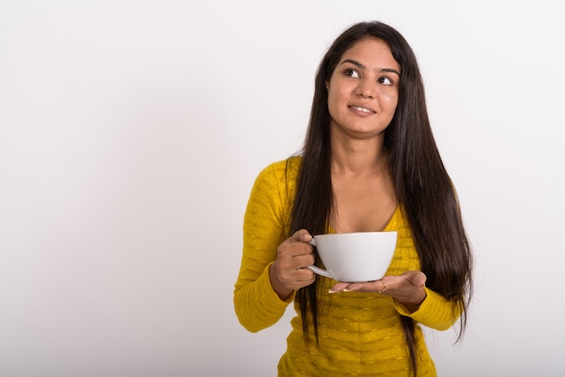 Giovane donna felice sorridendo e pensando mentre si tiene la tazza di caffè