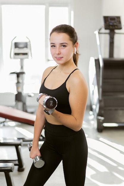 Giovane donna fitness che si esercita con manubri in palestra