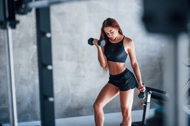 Giovane donna fitness è in palestra con manubri in mano.