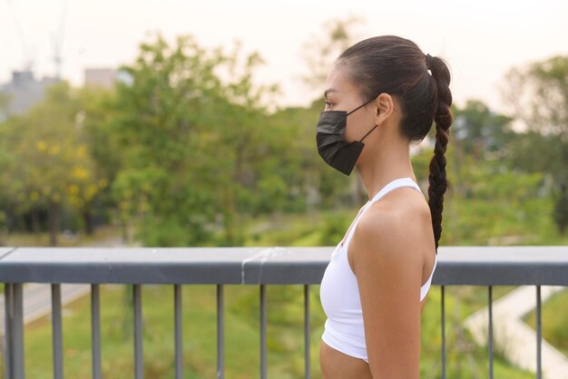 Giovane donna fitness in abbigliamento sportivo che indossa la maschera durante l'esercizio in città