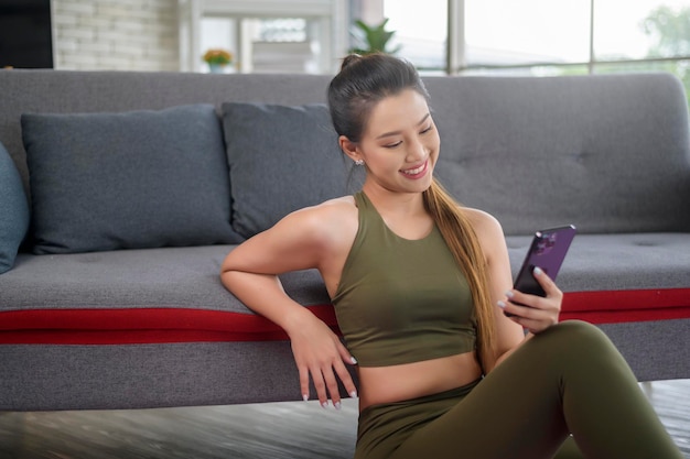 Giovane donna fitness in abbigliamento sportivo che utilizza lo smartphone mentre ti alleni a casa Salute e stili di vita