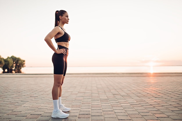 giovane donna fitness in piedi sulla spiaggia all'alba?