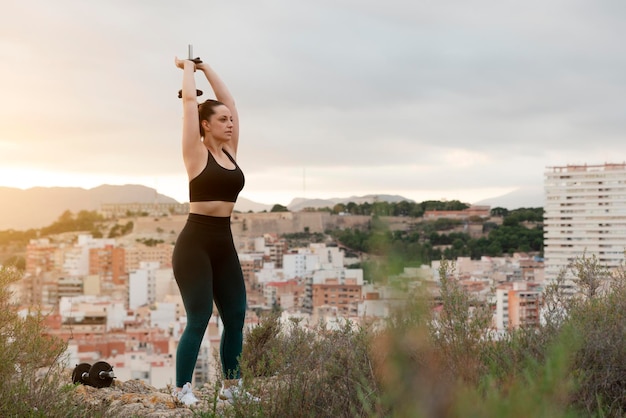 Giovane donna fitness solleva pesi all'aperto al tramonto