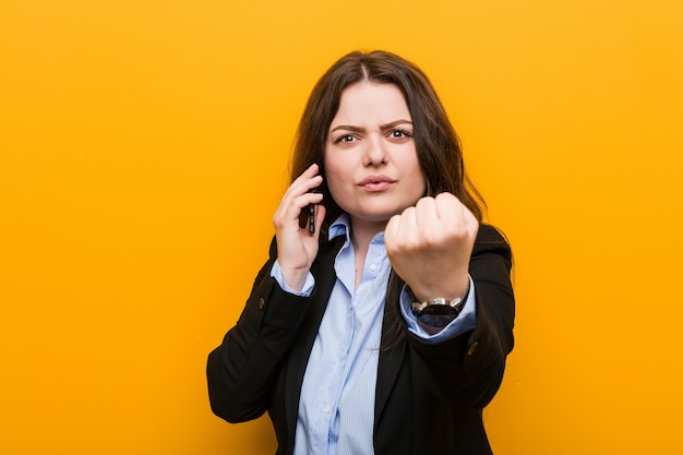 Giovane donna formosa plus size in possesso di un telefono che mostra il pugno, espressione facciale aggressiva.