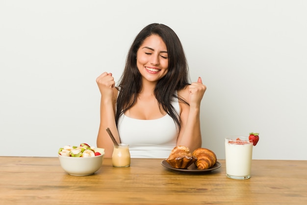 Giovane donna formosa prendendo una colazione alzando il pugno, sentendosi felice e di successo