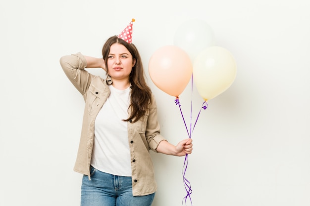 Giovane donna formosa taglie forti che celebra un compleanno toccando il dorso della testa, pensando e facendo una scelta.