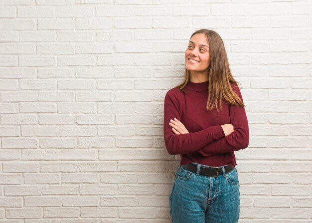 Giovane donna fresca su un muro di mattoni sorridente fiducioso e incrocio le braccia, guardando in alto