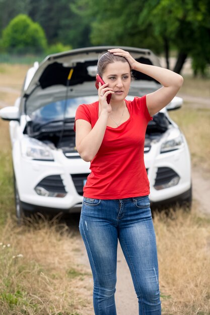 Giovane donna frustrata che chiede aiuto con la sua auto rotta