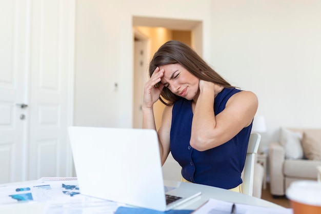 Giovane donna frustrata che lavora alla scrivania davanti al computer portatile che soffrono di mal di testa quotidiani cronici
