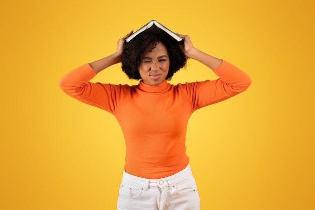 Giovane donna frustrata con una grimace che equilibra un libro sulla testa