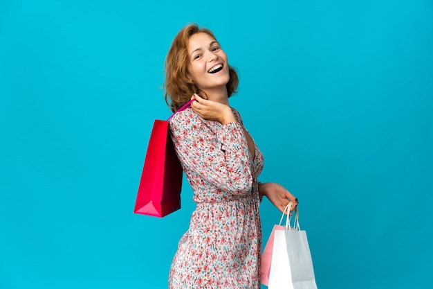 Giovane donna georgiana con il sacchetto della spesa isolato sulla parete blu che tiene i sacchetti della spesa e sorridente