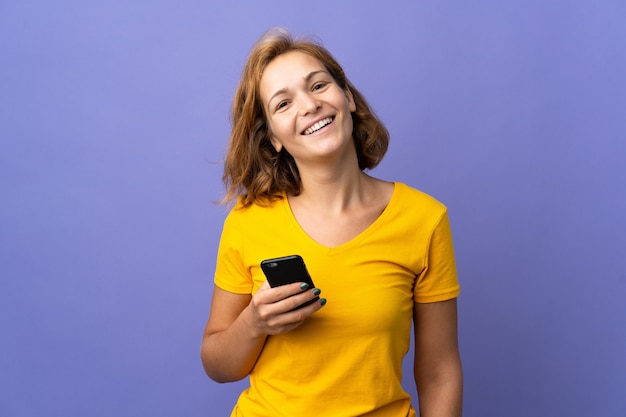 Giovane donna georgiana isolata sulla parete viola utilizzando il telefono cellulare