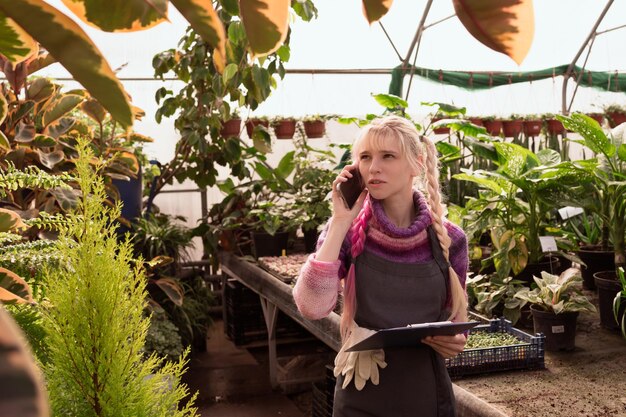 Giovane donna giardiniere con capelli rosa che indossa un grembiule e tiene in mano un tablet per scrivere e penna dentro