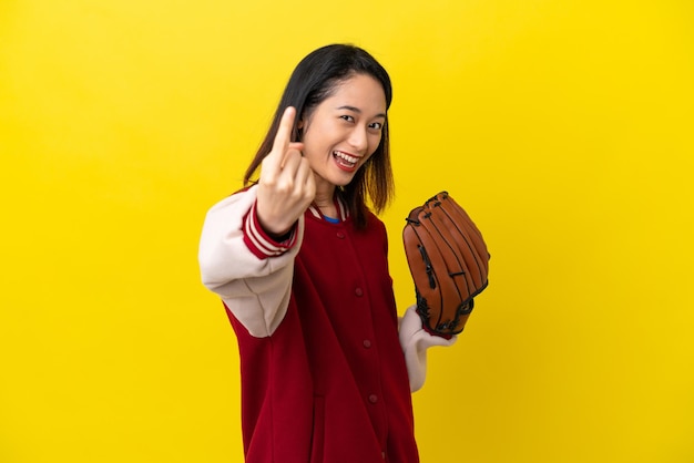 Giovane donna giocatore vietnamita con guanto da baseball isolato su sfondo giallo che fa il gesto in arrivo