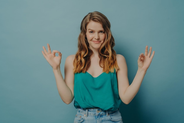 Giovane donna gioiosa sicura in abiti casual che gesturing segno giusto con entrambe le mani in studio