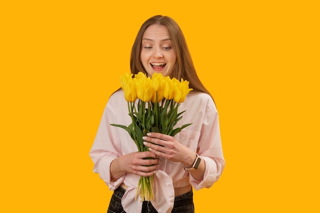 Giovane donna gioisce in mazzi di tulipani Ragazza con fiori gialli nelle sue mani isolato su sfondo giallo