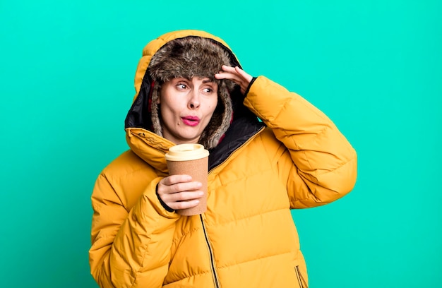 Giovane donna graziosa adulta che indossa giacca a vento e cappello invernale e tiene un caffè da asporto