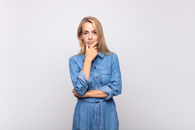 Giovane donna graziosa bionda premurosa con il vestito dal jeans