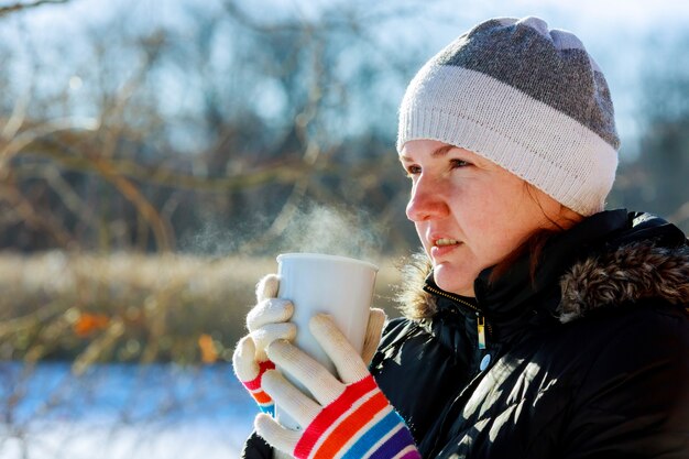 Giovane donna graziosa che beve tè caldo un giorno di inverno freddo