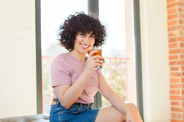 Giovane donna graziosa che beve una cola nella nuova casa