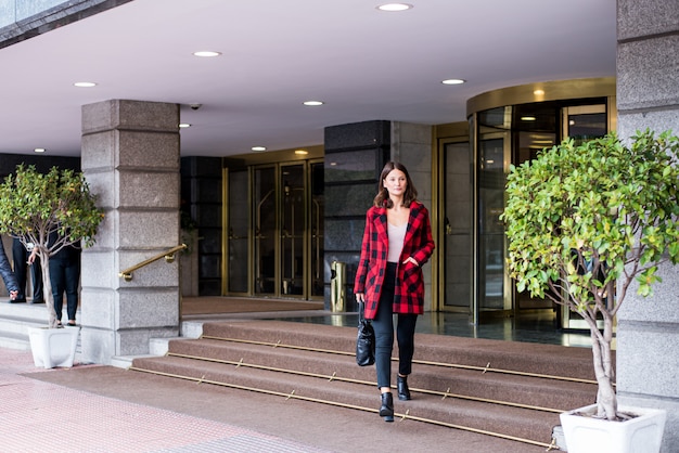 Giovane donna graziosa che cammina lasciando un hotel che indossa i vestiti eleganti di autunno