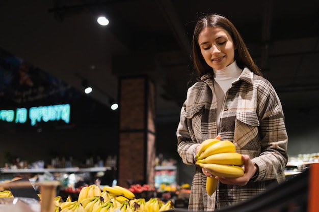 Giovane donna graziosa che compra banane al supermercato