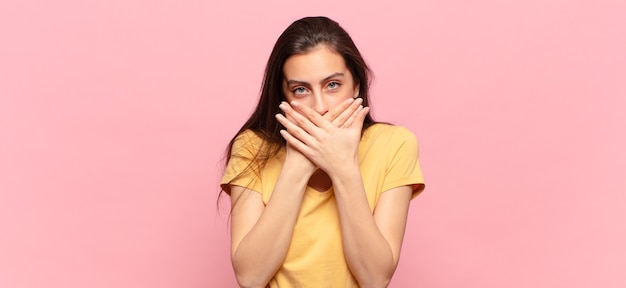 Giovane donna graziosa che copre la bocca con le mani