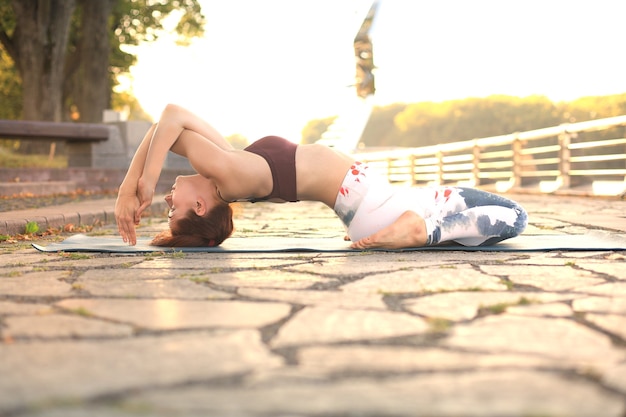 Giovane donna graziosa che fa esercizi di yoga nel parco.