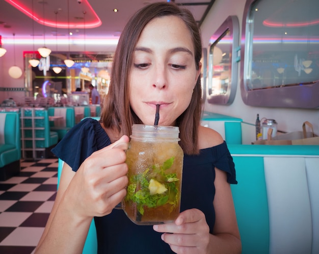 Giovane donna graziosa che ha un cocktail mojito fresco in un ristorante