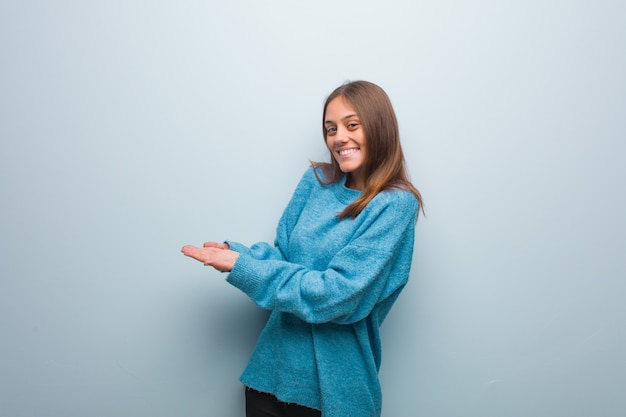 Giovane donna graziosa che indossa un maglione blu che tiene qualcosa con le mani