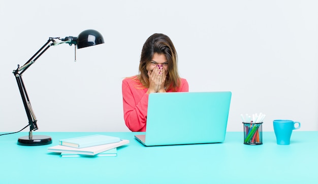 Giovane donna graziosa che lavora con un computer portatile che sembra bocca di copertura felice, allegra, fortunata e sorpresa con entrambe le mani