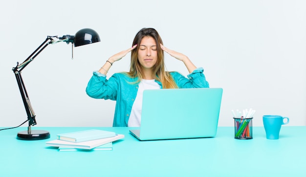 Giovane donna graziosa che lavora con un computer portatile che sembra concentrato, premuroso e ispirato, brainstorming e che immagina con le mani sulla fronte