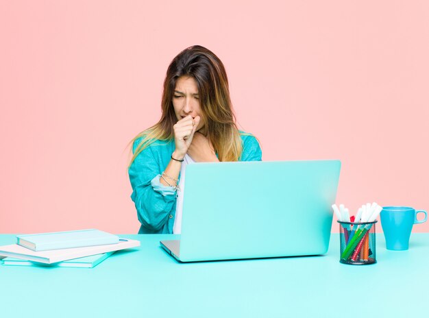 Giovane donna graziosa che lavora con un computer portatile sentirsi male con mal di gola e sintomi influenzali, tossendo con la bocca coperta