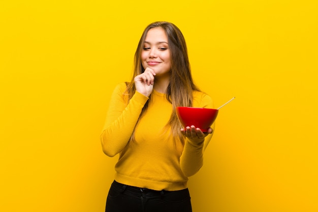 Giovane donna graziosa che mangia prima colazione contro la parete arancio